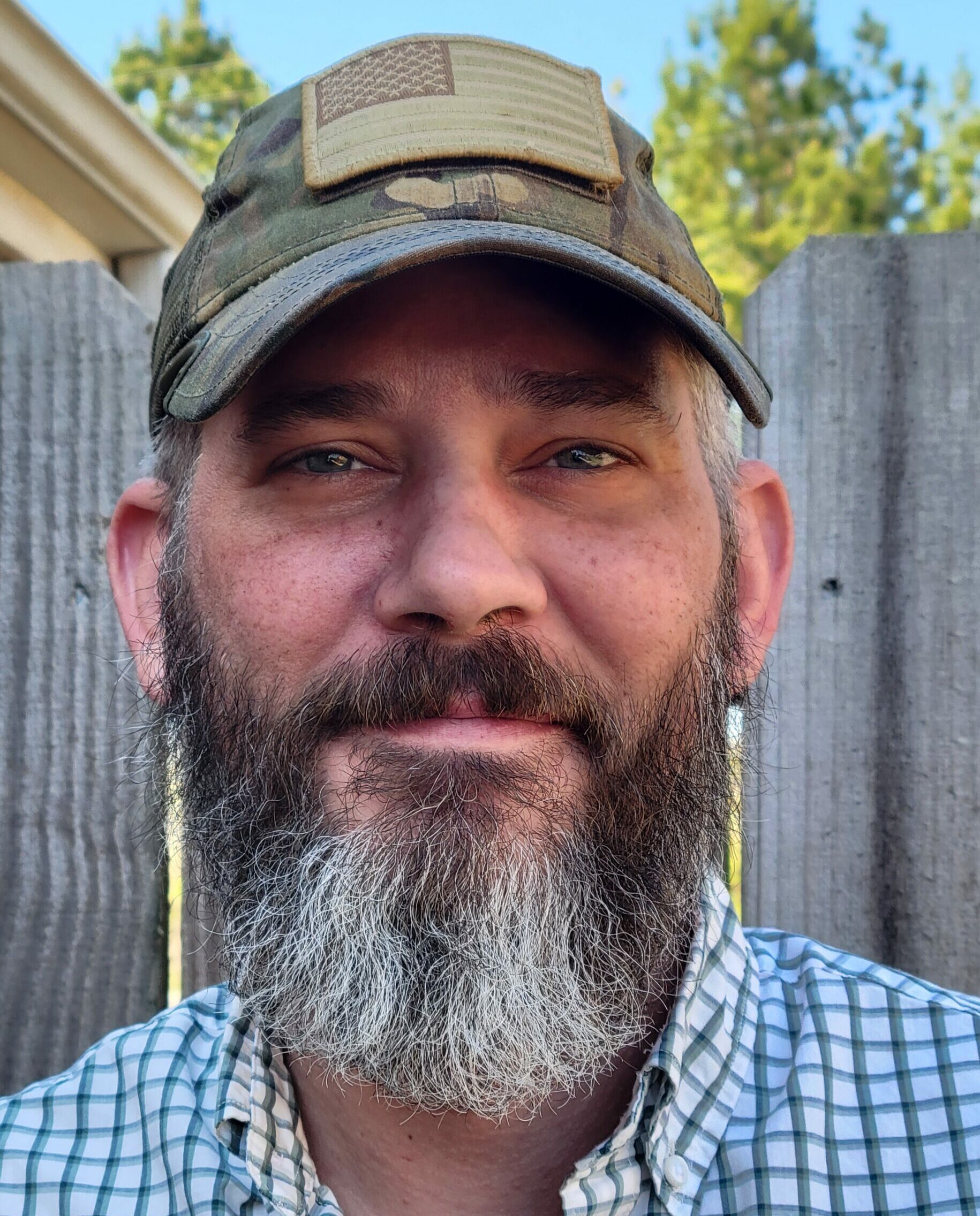 Bearded man wearing cap in front of wooden fence